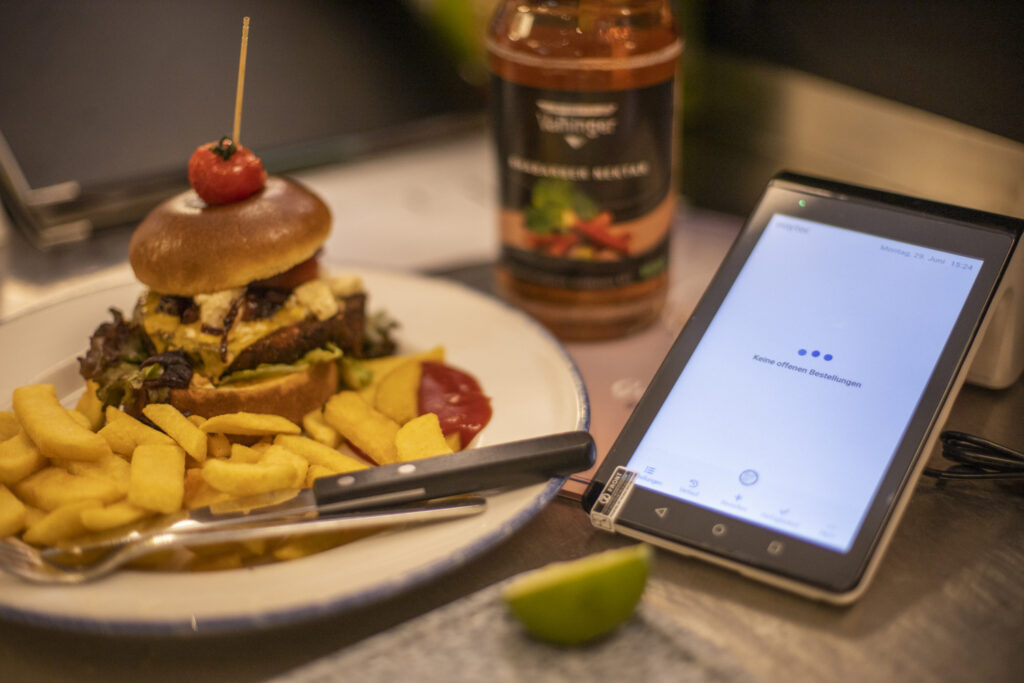Man sieht ein Essen und daneben ein Gerät über das die Bestellungen digital verwaltet werden.